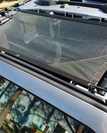 Car roof with black netting sunshade, secured with clips, protecting against sun and debris on a sunny day.