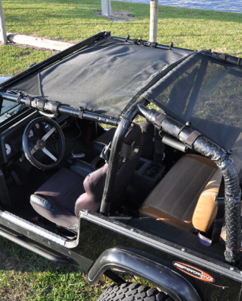 Off-road black Jeep with sunshade, open-top seats, near waterfront in grassy area.