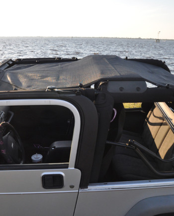 Convertible jeep parked by a serene lake under a clear sky, interior view with black and gray seating.