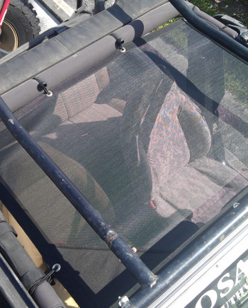 Jeep with black mesh roof cover, parked under sunlight, interior seats visible through mesh.