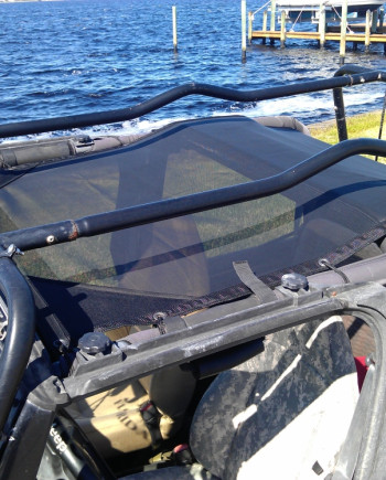 Jeep with netted roof parked by a lake on a sunny day, showcasing off-road readiness and scenic waterside view.