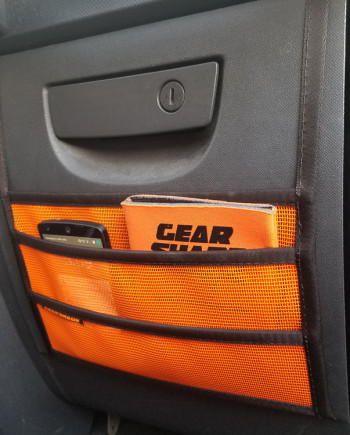 Car door storage with orange mesh pockets holding a booklet and a smartphone.