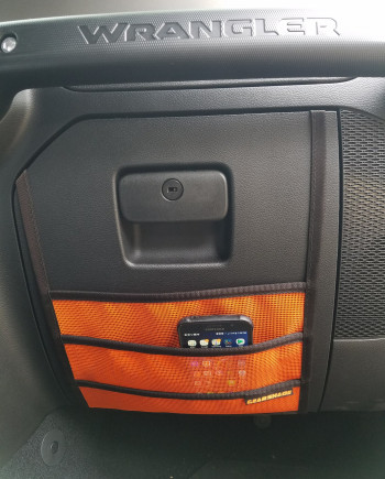 Jeep Wrangler interior with an orange mesh storage pocket and smartphone inside, showcasing vehicular design and functionality.