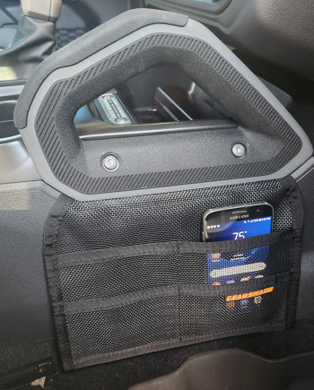 Car seat organizer holding a smartphone displaying "75°," installed on a vehicle's side with a gear shift nearby.