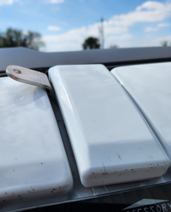Close-up of a white SUV roof hinge under a blue sky with scattered clouds.